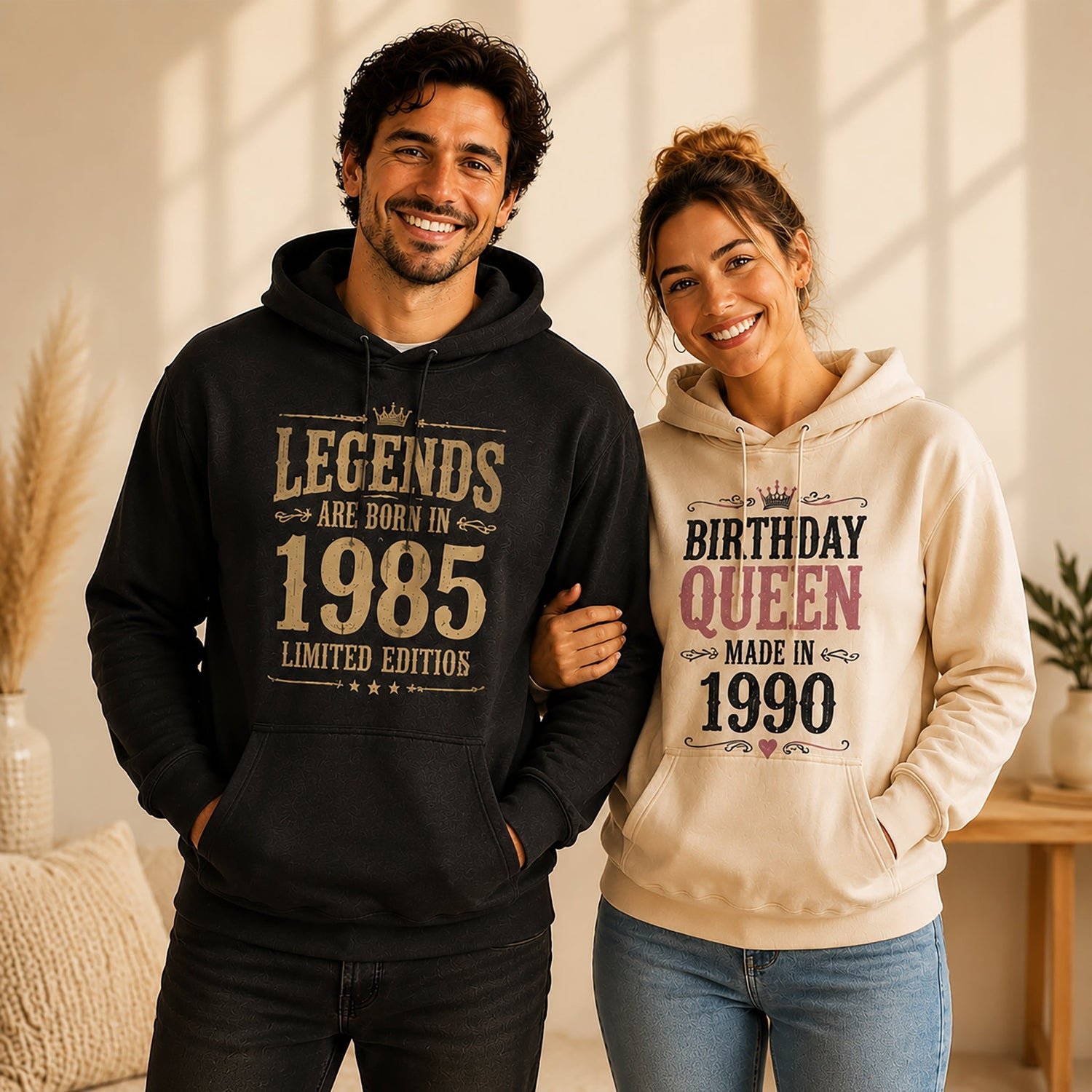 A smiling couple stands closely together in a warm, softly lit indoor setting, wearing matching custom birthday hoodies with vintage-inspired text designs, conveying a cozy, affectionate, and celebratory mood.